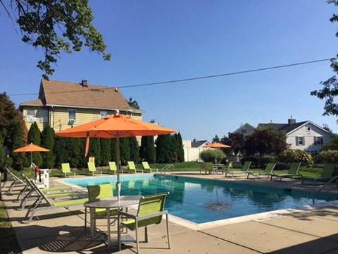 A pool with chairs and umbrellas in front of a house.