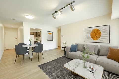 A modern living room with a grey sofa, a dining table with chairs, and a coffee table with a vase on it.