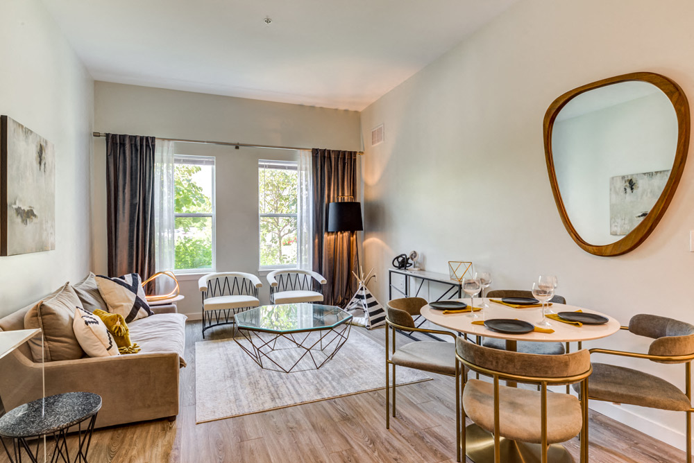 A modern living room with a glass coffee table and a round mirror on the wall.