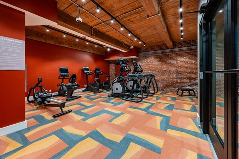 A gym with a variety of exercise equipment and a colorful floor at The Cordovan at Haverhill Station, Haverhill, MA