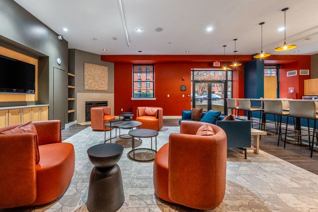 A room with orange chairs and a television on the wall at The Cordovan at Haverhill Station, Haverhill, MA