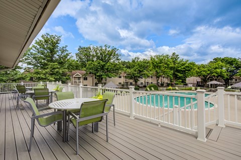 A wooden deck with a table and chairs overlooking a pool at Williamsburg Estates, Harrisburg, PA, 17112