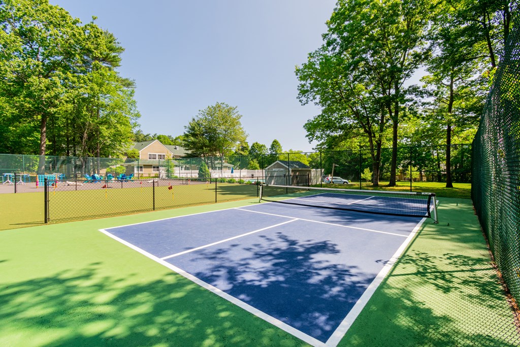 A tennis court surrounded by a fence and trees at at Mariner's Hill Apartments, Massachusetts.