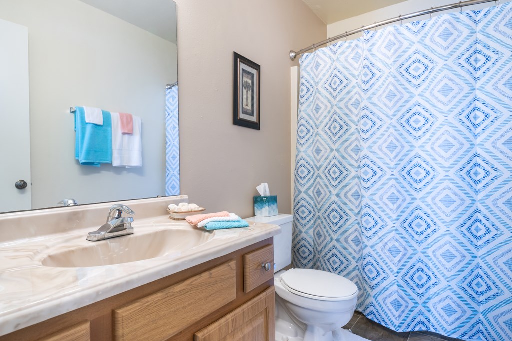 A bathroom with a toilet, sink, and shower curtain Fishermans Landing Apartments in Ormond Beach, FL.