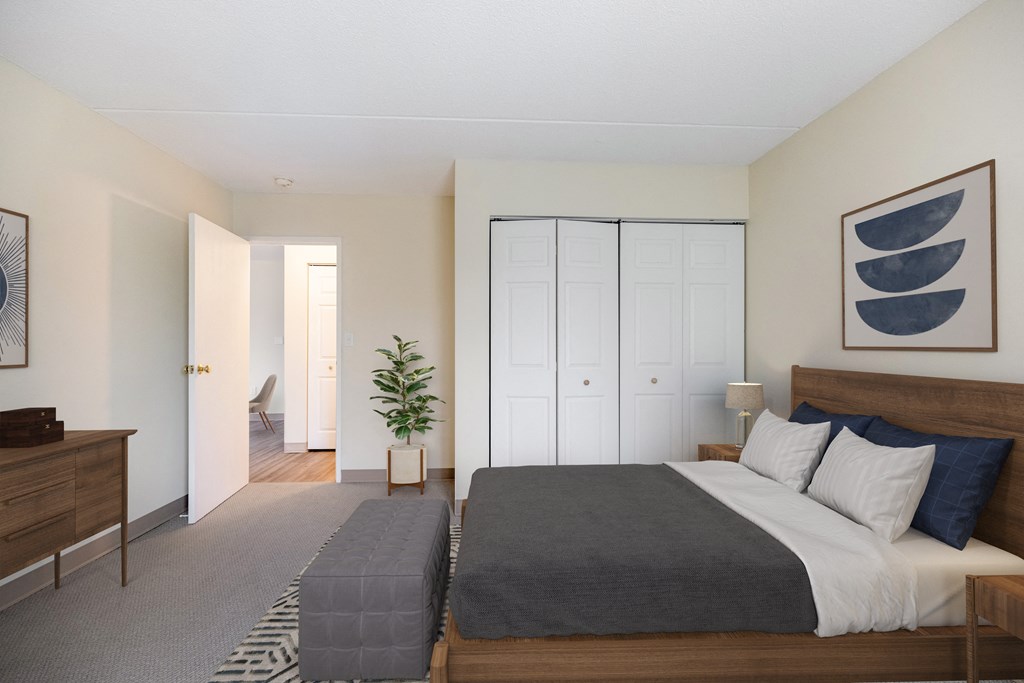 A bedroom with a bed and a dresser and a closet at North Stoughton Village Apartments in Stoughton, MA