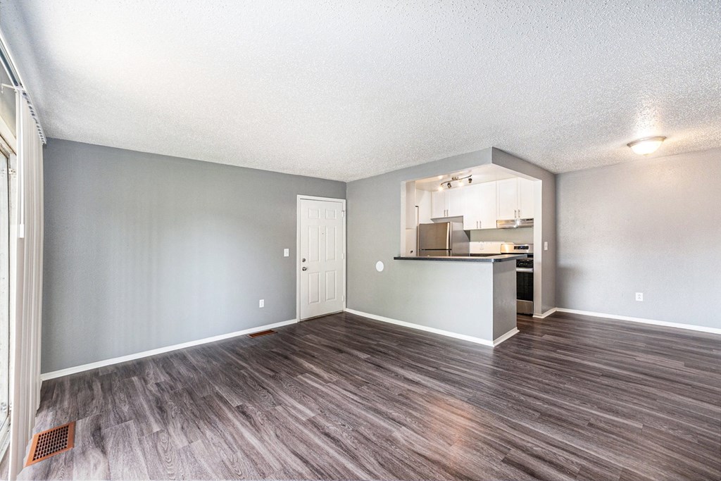 an empty living room with a kitchen in the background