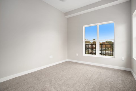 A room with a carpeted floor and a window showing a view of houses and trees.