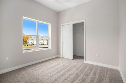 A room with a carpeted floor and a large window showing a view of a street with houses.