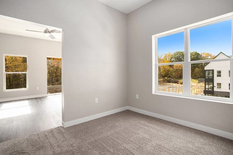 A room with a carpet floor, a ceiling fan, and a window showing an outdoor view.