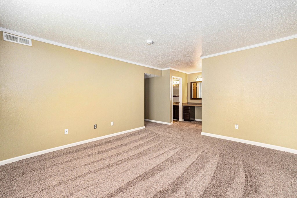 a living room with a carpeted floor and a kitchen in the background