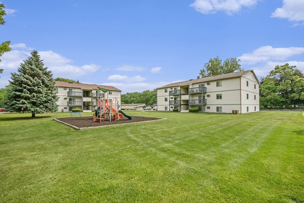 a playground in the middle of a grass field next to an apartment building