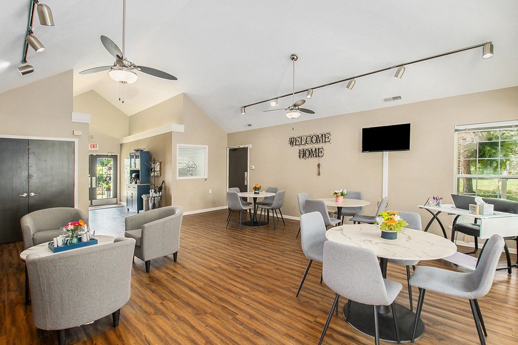 a living room with tables and chairs and a kitchen with a tv