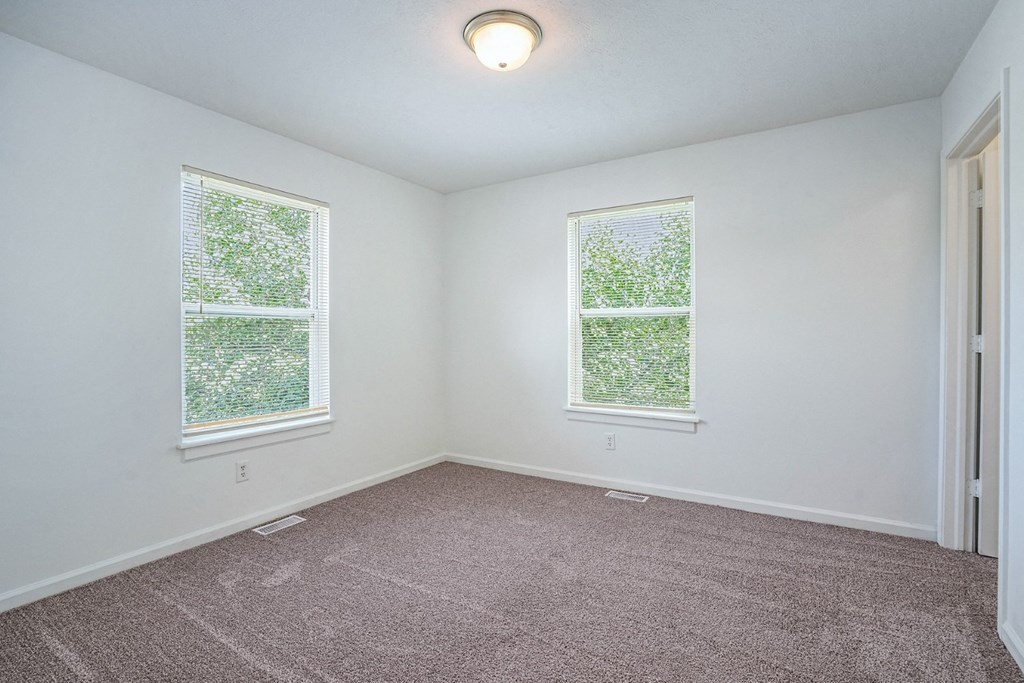 a bedroom with two windows and a carpeted floor