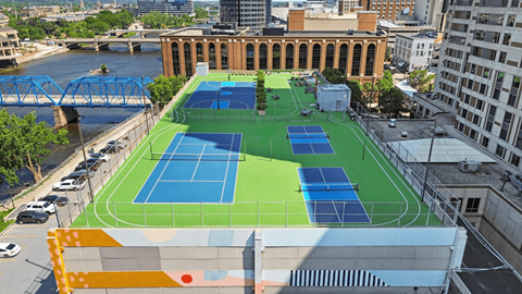A tennis court is located on a rooftop with a river and buildings in the background.