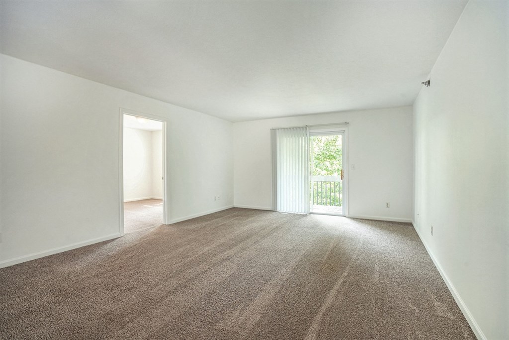a spacious living room with white walls and carpet