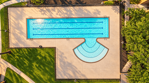 An aerial view of a swimming pool surrounded by a concrete floor and a grassy area.