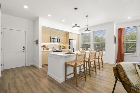 A kitchen with wooden floors and a white island with chairs around it.