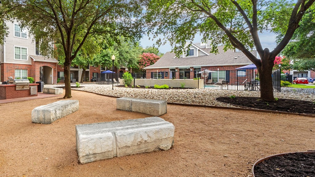 A playground with a red dirt surface and a few trees.