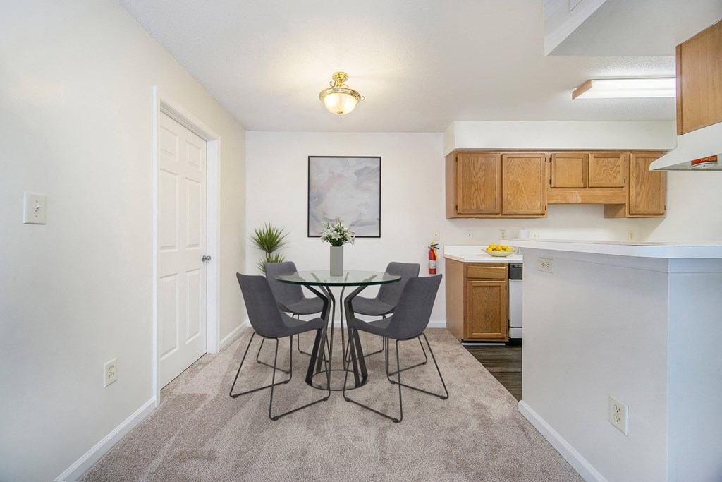 a dining area with a glass table and chairs and a kitchen