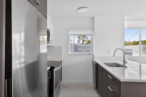 A modern kitchen with a stainless steel refrigerator and a window overlooking a tree-lined street.