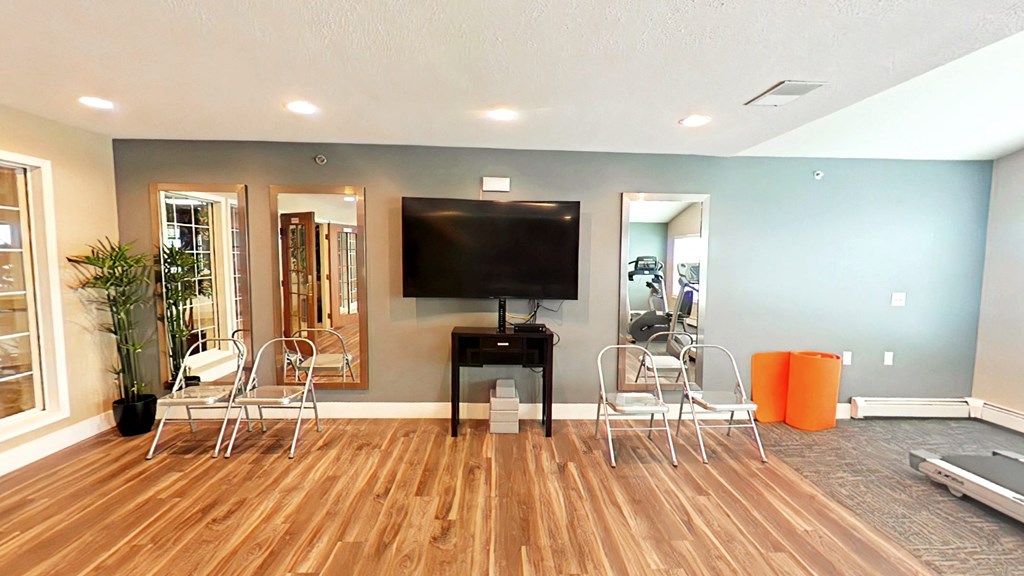 A living room with a wooden floor and a television mounted on the wall.