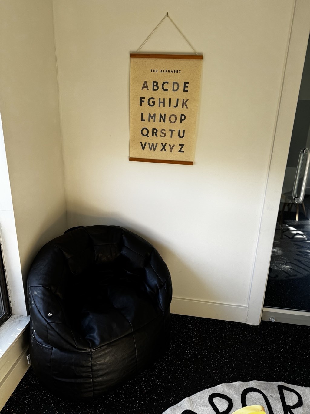 A black bean bag chair sits under a poster of the alphabet.
