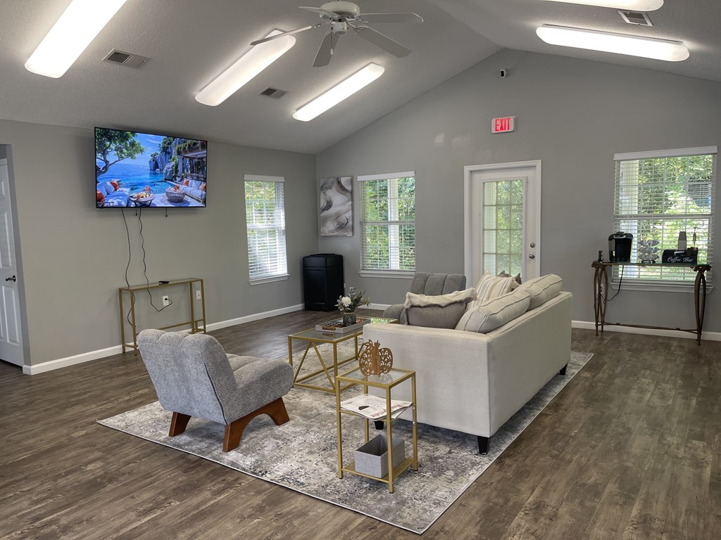 A living room with a grey sofa, a grey armchair, a white couch, and a TV mounted on the wall.