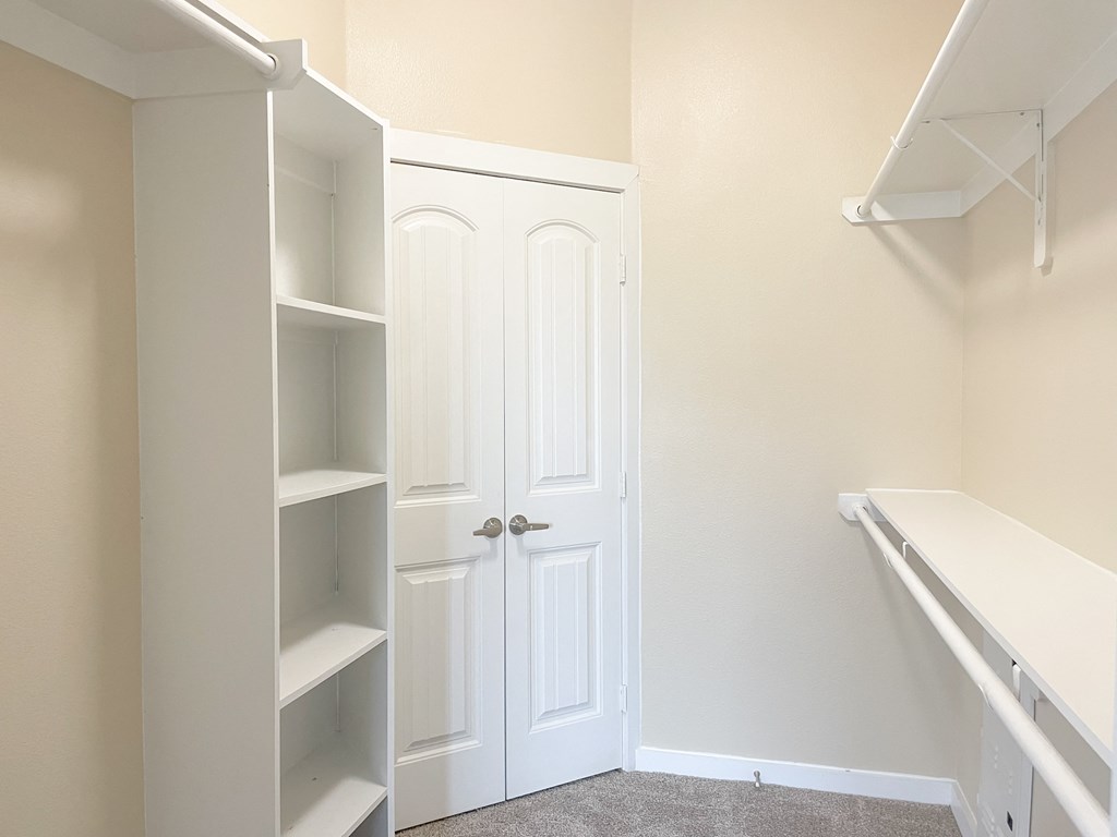 a walk in closet with a white closet door and white shelves
