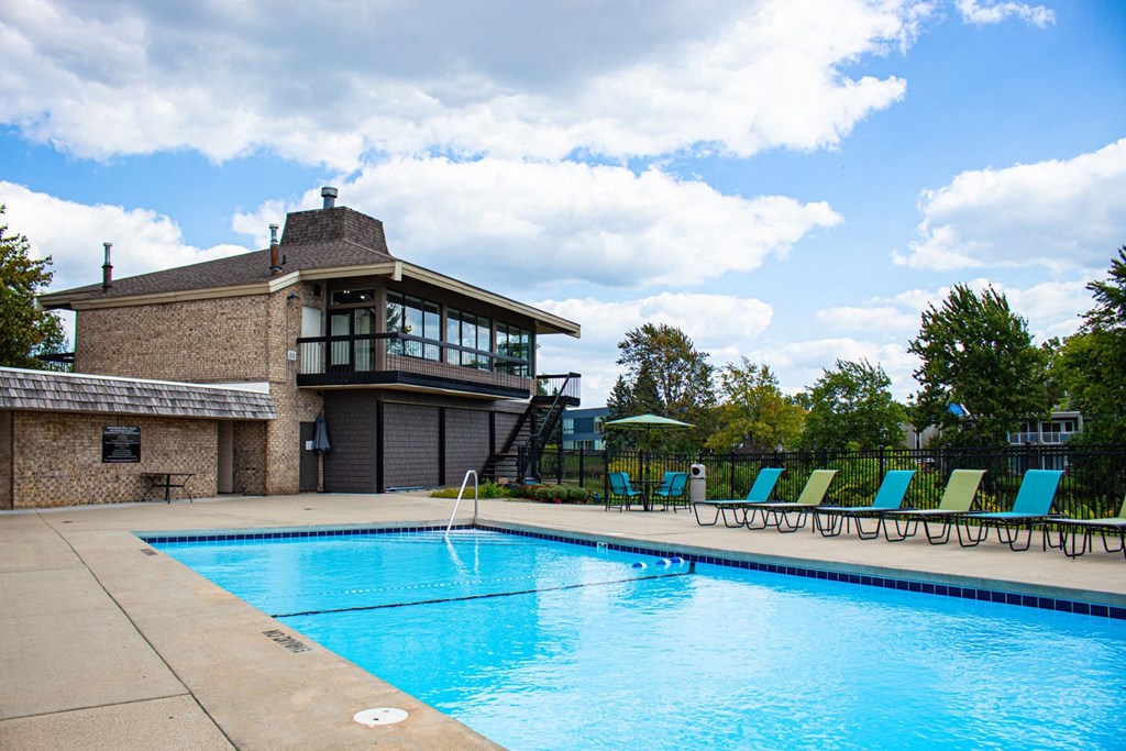 a swimming pool in front of a building with green chairs