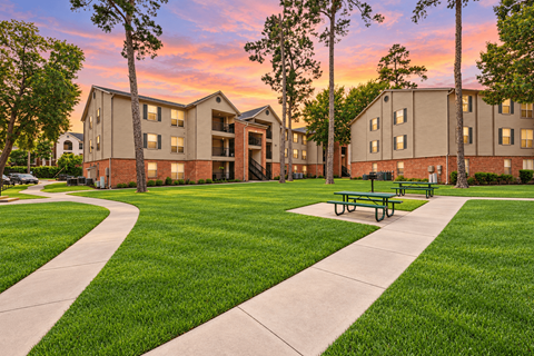 A sunset view of apartment buildings with a green lawn in the foreground.