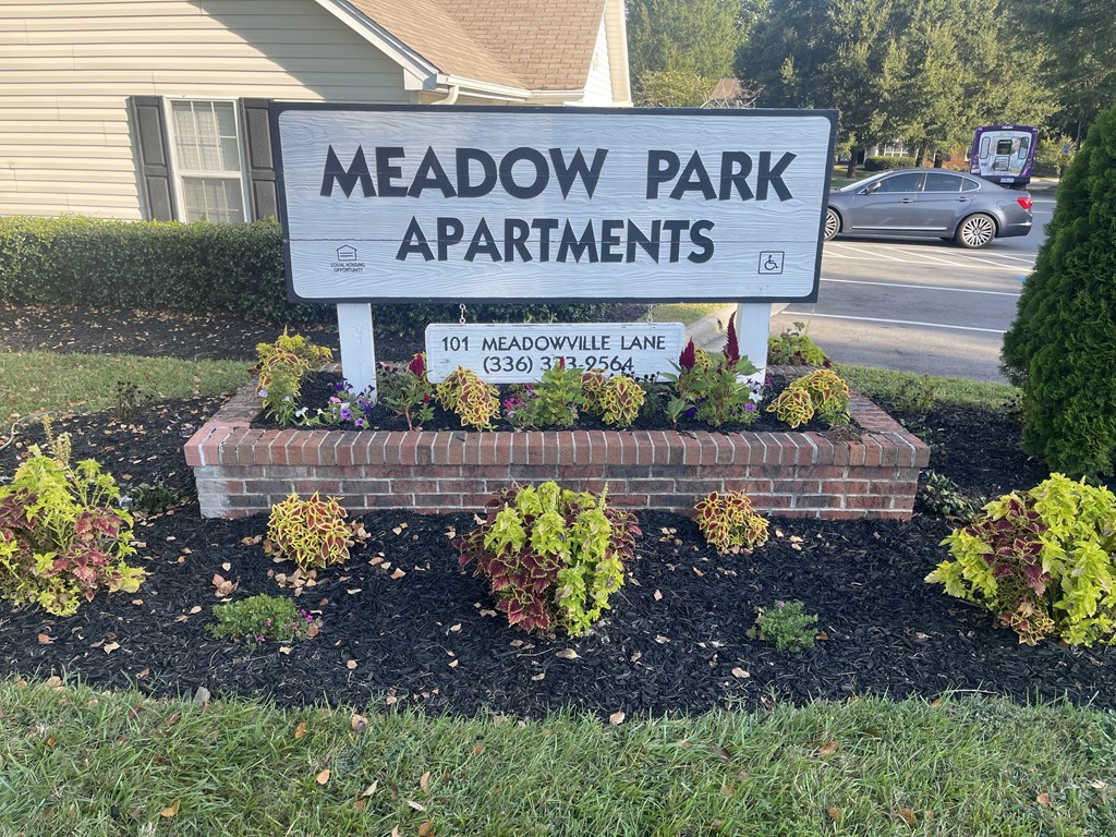 A sign for Meadow Park Apartments is displayed in front of a house.