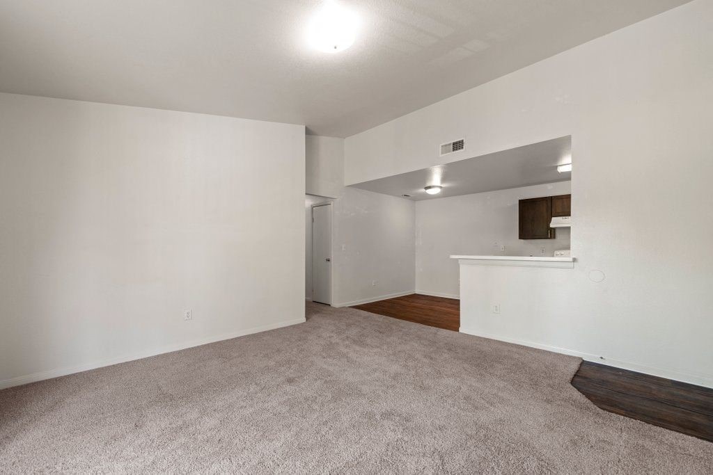 an empty living room with a kitchen in the background