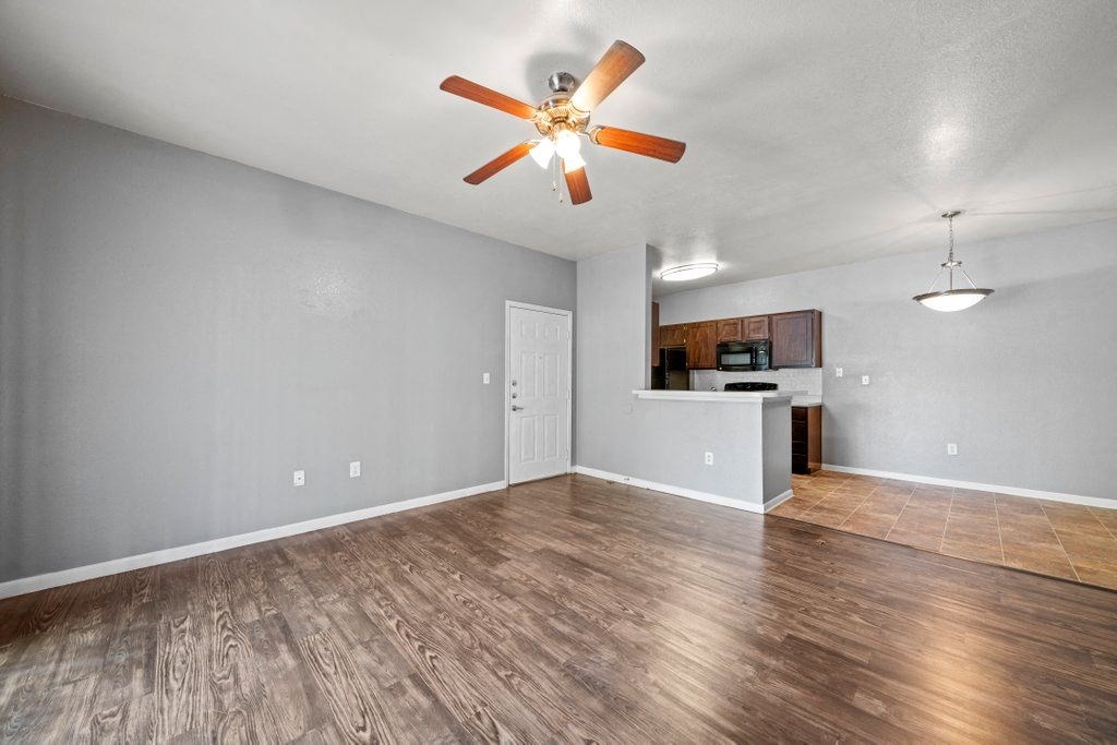 an empty living room with a ceiling fan and a kitchen in the background