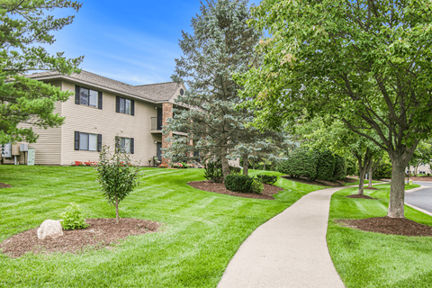 a walkway through a grassy area with trees and a building in the background