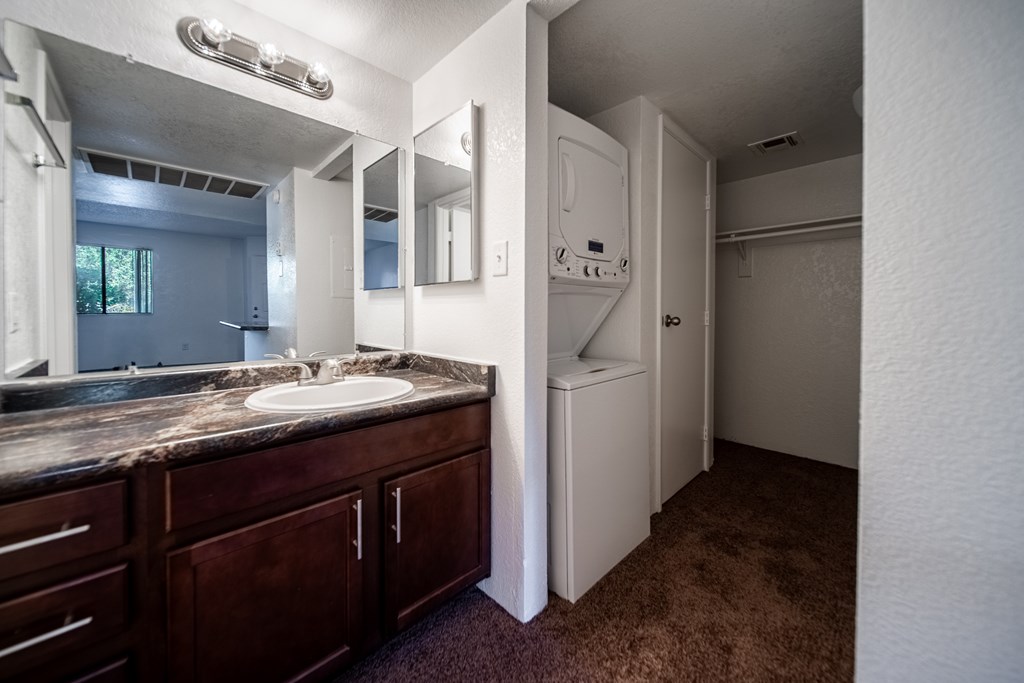 A bathroom with a sink, mirror, and a washer and dryer.