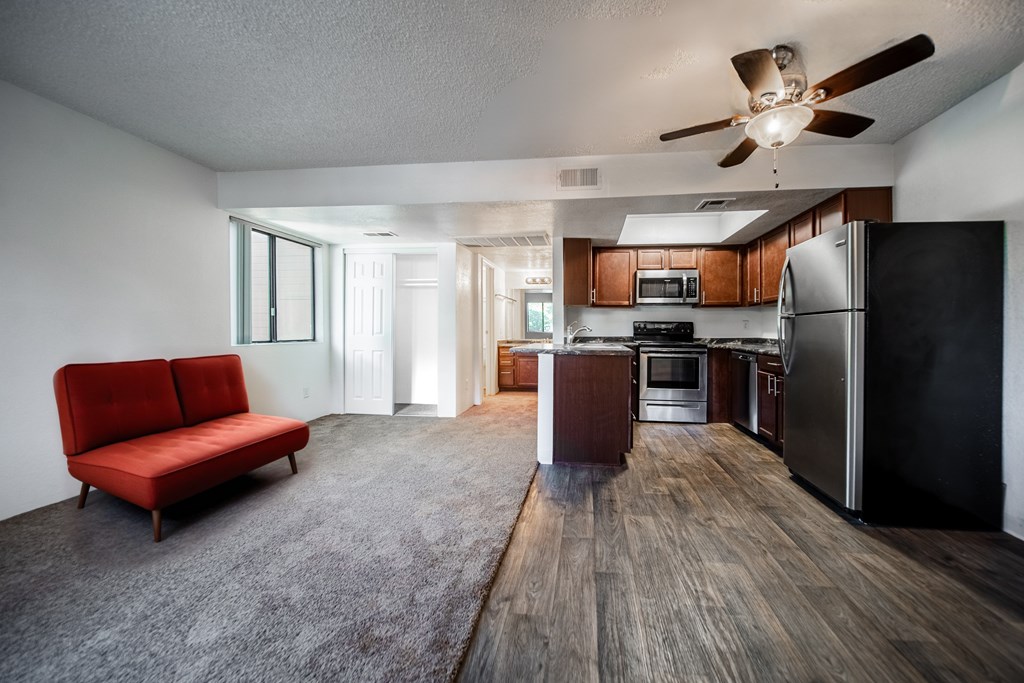 A red couch sits in a spacious kitchen and living room with wood flooring and modern appliances.