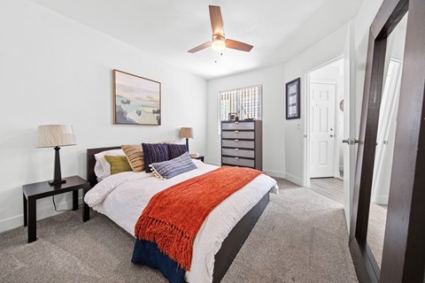 A bedroom with a bed, a ceiling fan, and a painting on the wall.