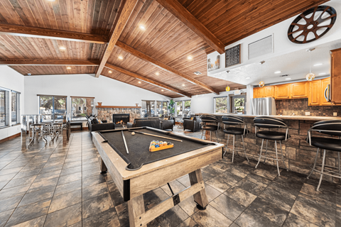 A billiard table is in the middle of a room with a bar and stools.