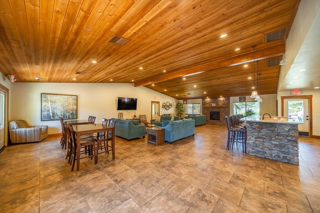 A spacious living room with a stone fireplace and wooden ceiling.