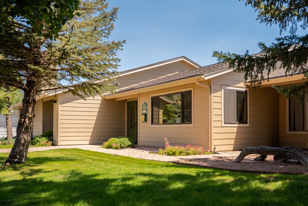 A house with a brown siding and a tan roof with a small garden in front.