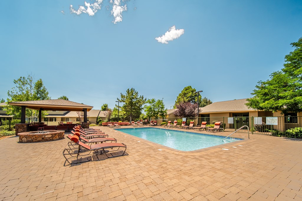 A pool surrounded by a brick patio with chairs and a building in the background.