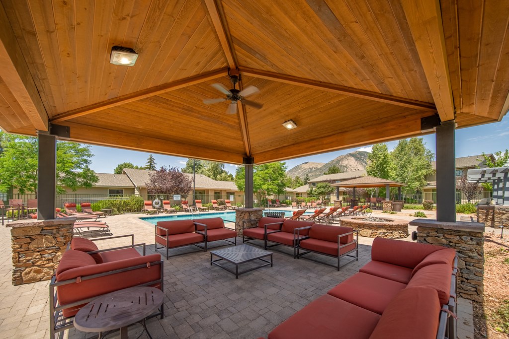 A patio with a table and chairs under a wooden roof.