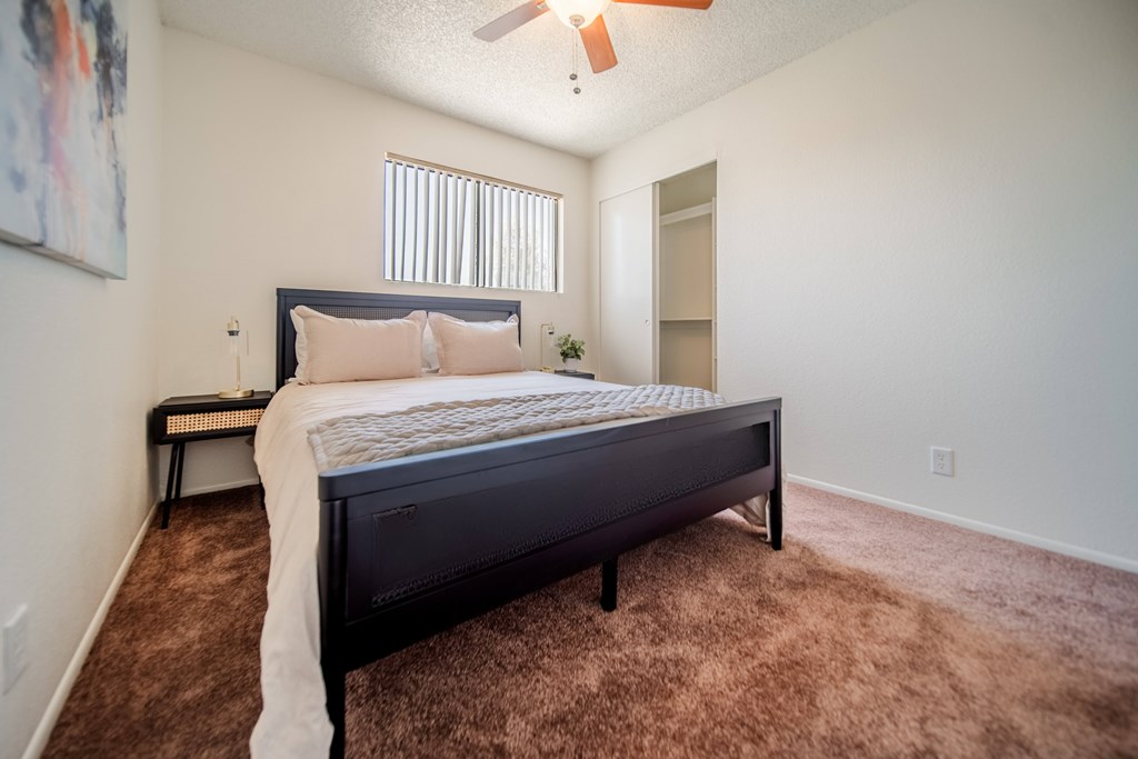 A bedroom with a bed, carpet, and a ceiling fan.