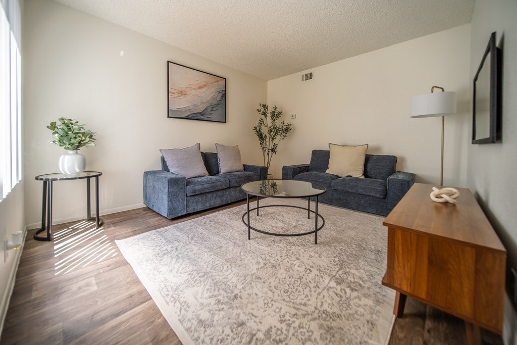 A living room with a grey couch, a blue couch, a round table, and a wooden coffee table.