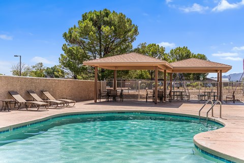 A pool with a sunshade and lounge chairs.