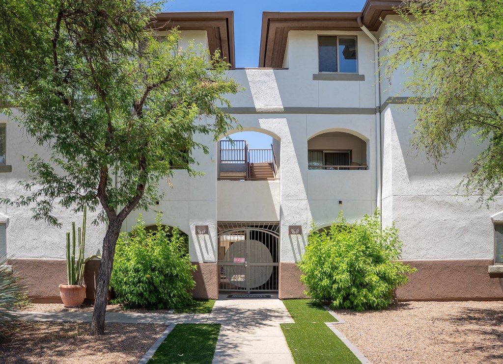 A white building with a gate in the middle of a landscaped yard.