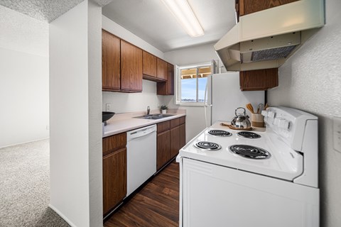 A white stove top oven with four burners is in a kitchen with wooden cabinets.