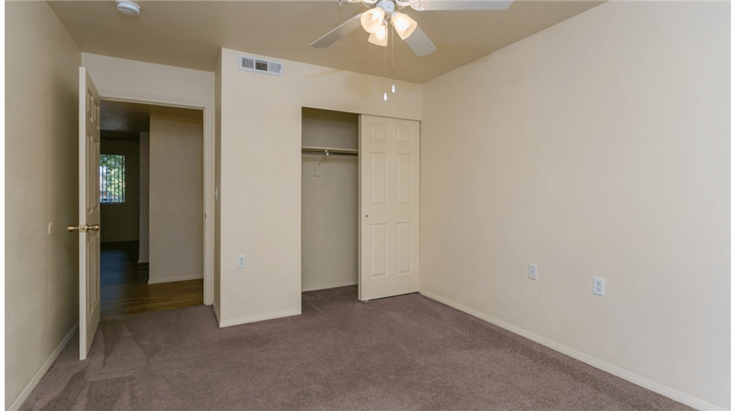 an empty living room with a closet and a ceiling fan