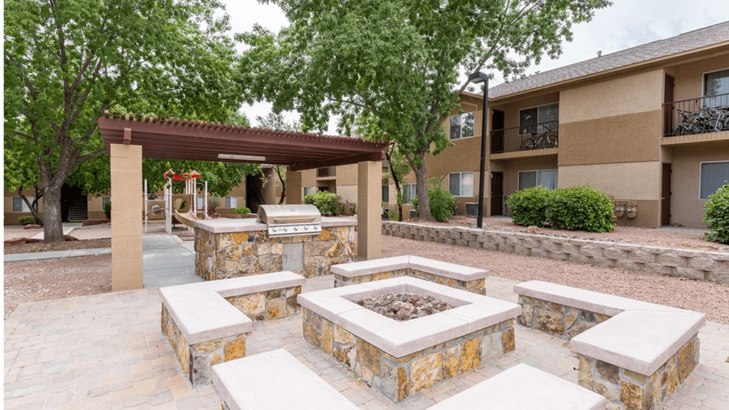 a patio with a fire pit and benches in front of an apartment building