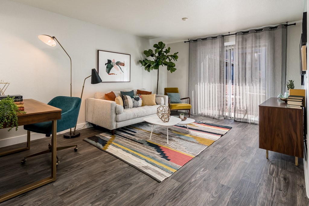 a living room with a couch chair and desk in front of a sliding glass door